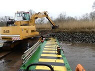 Das Uferdeckwerk wird mithilfe eines auf einem Ponton stehenden gelben Baggers abgetragen